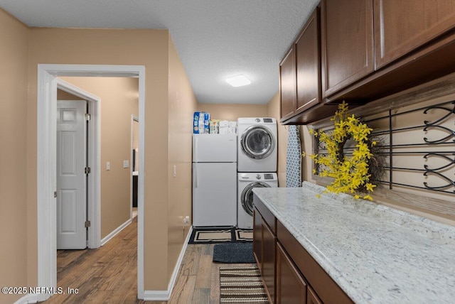 kitchen with a textured ceiling, stacked washer and dryer, wood finished floors, baseboards, and freestanding refrigerator