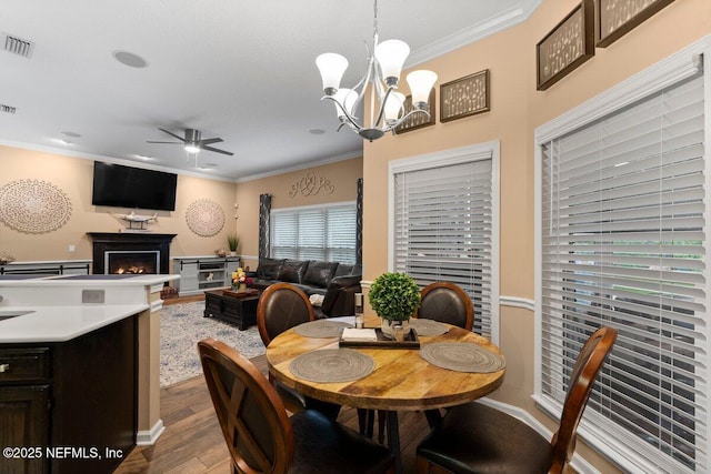 dining room with a warm lit fireplace, visible vents, and crown molding