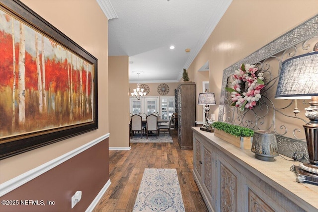 corridor featuring baseboards, ornamental molding, dark wood-style flooring, a textured ceiling, and a chandelier