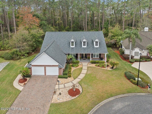 new england style home featuring a porch, decorative driveway, brick siding, and a front lawn