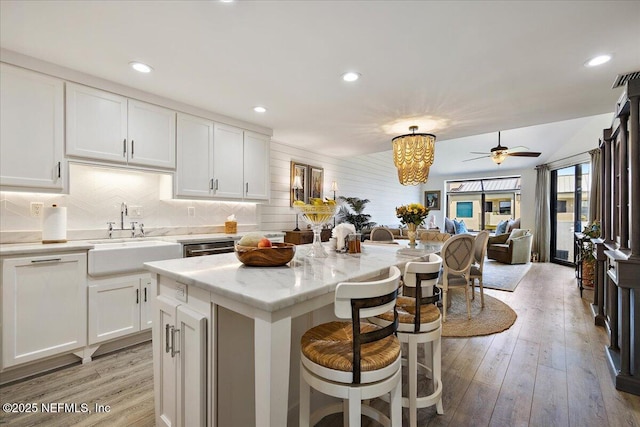 kitchen with a kitchen island, light wood-style flooring, a sink, white cabinets, and open floor plan