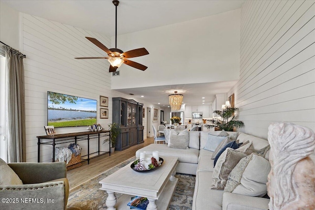 living area featuring wooden walls, light wood-style flooring, a high ceiling, and ceiling fan