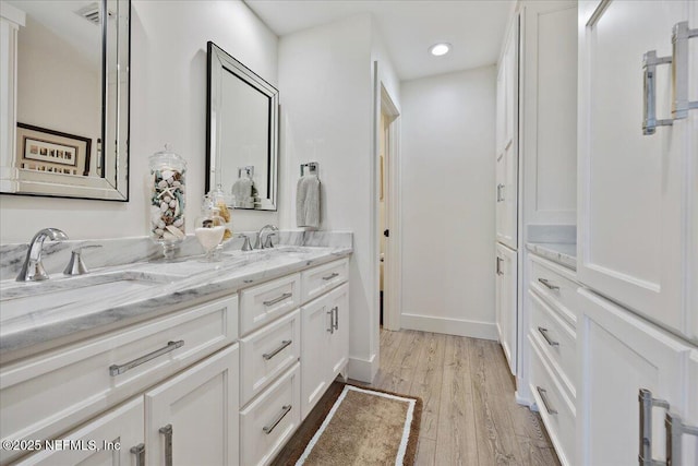 bathroom with a sink, baseboards, wood finished floors, and double vanity