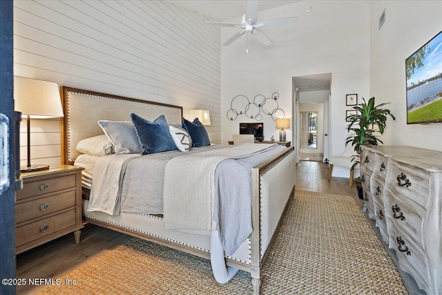 bedroom featuring visible vents, a high ceiling, wood finished floors, and wooden walls