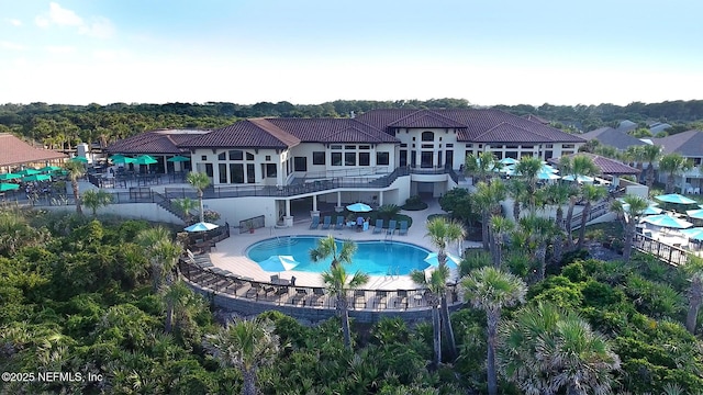 rear view of property featuring a patio area, stairway, a tile roof, and a community pool