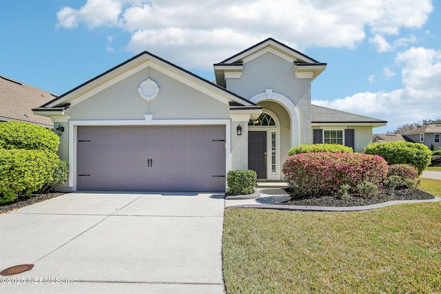 view of front of home with an attached garage, driveway, a front yard, and stucco siding