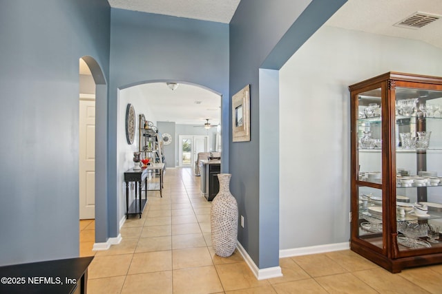 corridor featuring arched walkways, visible vents, baseboards, and light tile patterned floors