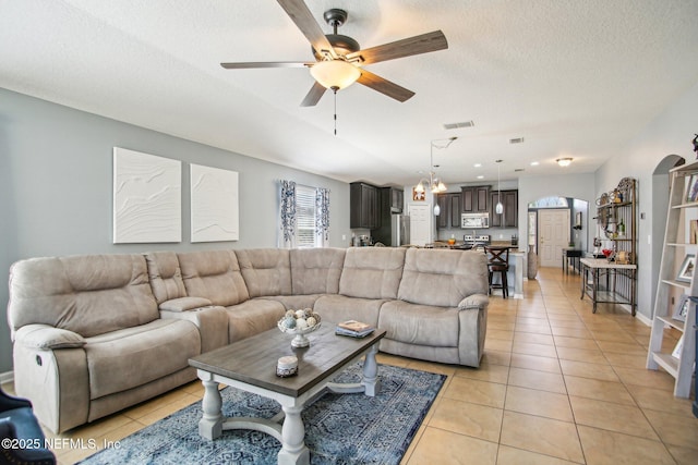 living room featuring light tile patterned floors, a textured ceiling, arched walkways, and a ceiling fan