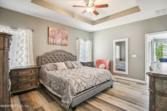 bedroom featuring a raised ceiling, visible vents, baseboards, and wood finished floors