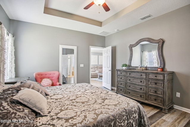 bedroom with baseboards, visible vents, ceiling fan, wood finished floors, and a tray ceiling