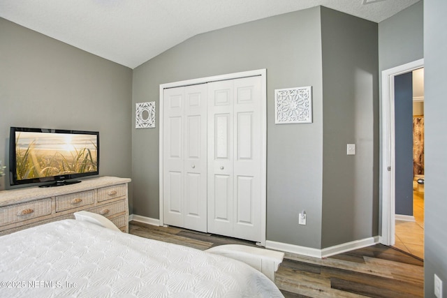 bedroom with a closet, vaulted ceiling, baseboards, and wood finished floors