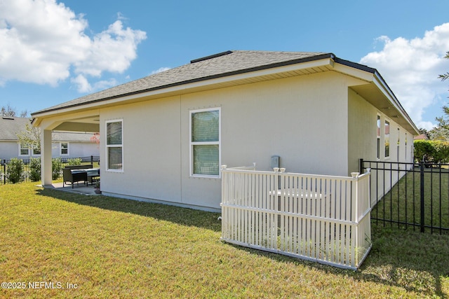 view of side of home with a shingled roof, fence, a yard, a patio area, and stucco siding