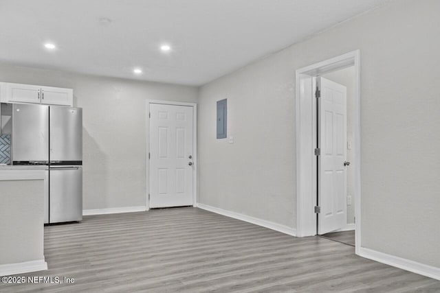 unfurnished dining area featuring baseboards, recessed lighting, light wood-style flooring, and electric panel