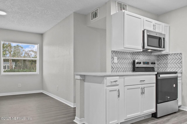 kitchen with visible vents, white cabinets, light countertops, appliances with stainless steel finishes, and tasteful backsplash