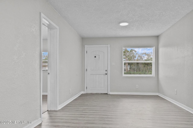 entryway with light wood-style floors, baseboards, a textured ceiling, and a textured wall