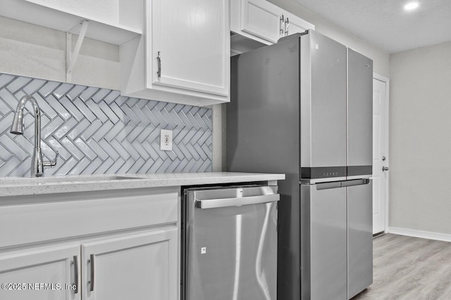 kitchen with light wood-style flooring, decorative backsplash, appliances with stainless steel finishes, white cabinets, and a sink