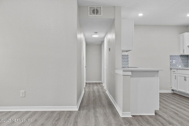 hall with baseboards, visible vents, and light wood finished floors