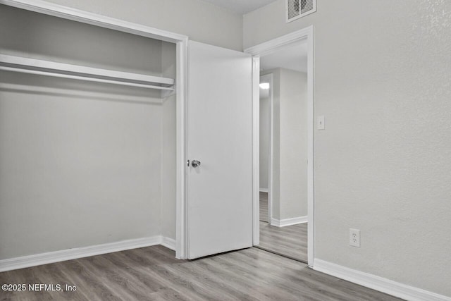 unfurnished bedroom featuring light wood-style floors, baseboards, visible vents, and a closet