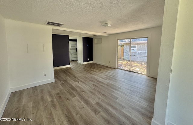 empty room featuring a textured ceiling, wood finished floors, visible vents, and baseboards