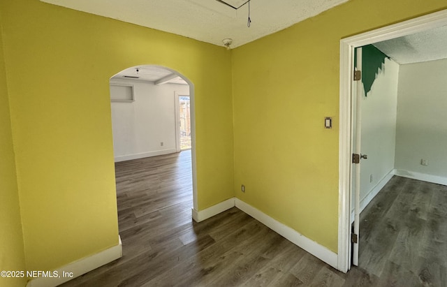 hall featuring arched walkways, dark wood-style flooring, and baseboards