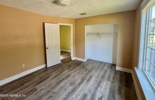 unfurnished bedroom featuring baseboards, visible vents, a closet, and wood finished floors