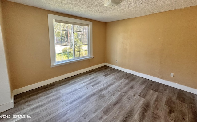 empty room featuring a textured ceiling, wood finished floors, and baseboards