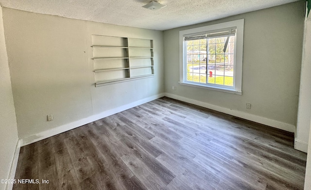 unfurnished room featuring a textured ceiling, wood finished floors, built in features, and baseboards