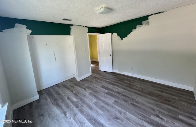 empty room with visible vents, a textured ceiling, baseboards, and wood finished floors