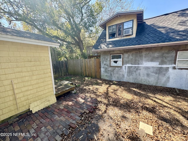 view of side of property with a shingled roof, fence, and a patio