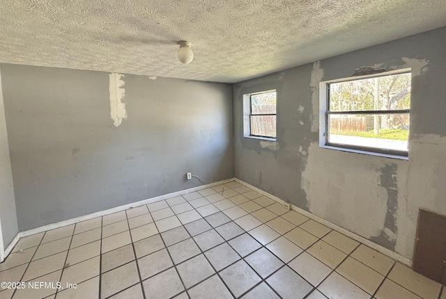 tiled empty room featuring a textured ceiling and baseboards