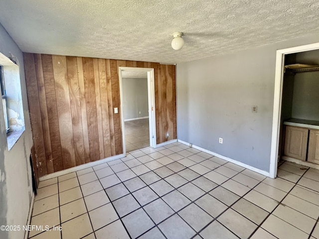 unfurnished bedroom with a textured ceiling, light tile patterned floors, baseboards, and wooden walls