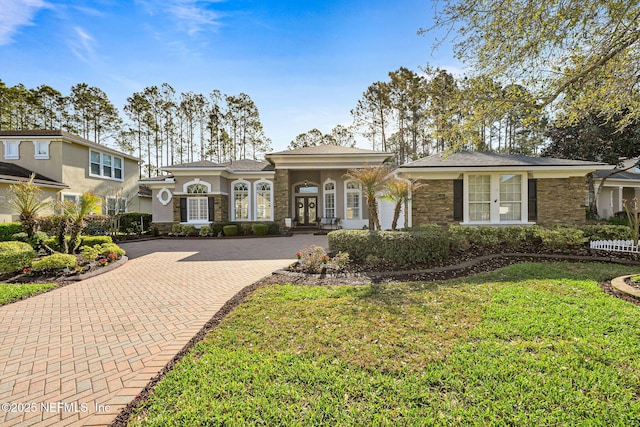 view of front of property with stone siding, french doors, decorative driveway, stucco siding, and a front yard