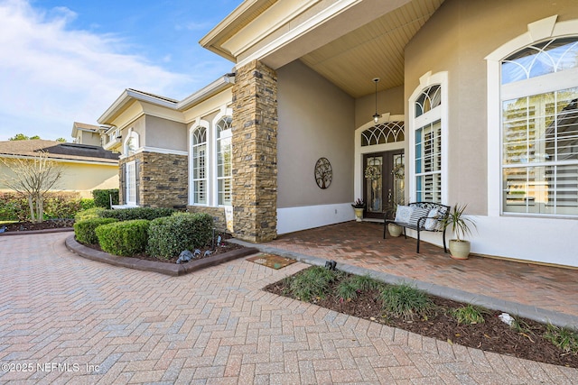 view of exterior entry featuring stone siding, french doors, and stucco siding