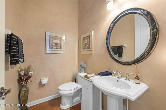 half bathroom featuring toilet, a sink, baseboards, and wood finished floors