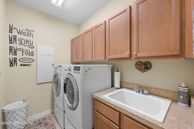 clothes washing area with a textured ceiling, washing machine and dryer, a sink, baseboards, and cabinet space