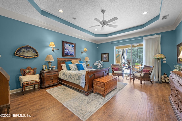 bedroom featuring a textured ceiling, wood finished floors, visible vents, baseboards, and a raised ceiling