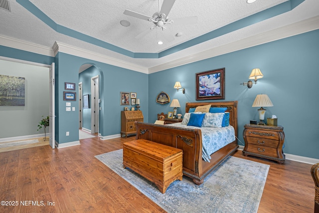 bedroom featuring arched walkways, a textured ceiling, wood finished floors, and baseboards