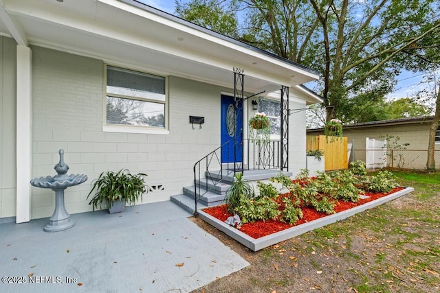 doorway to property featuring concrete block siding and fence