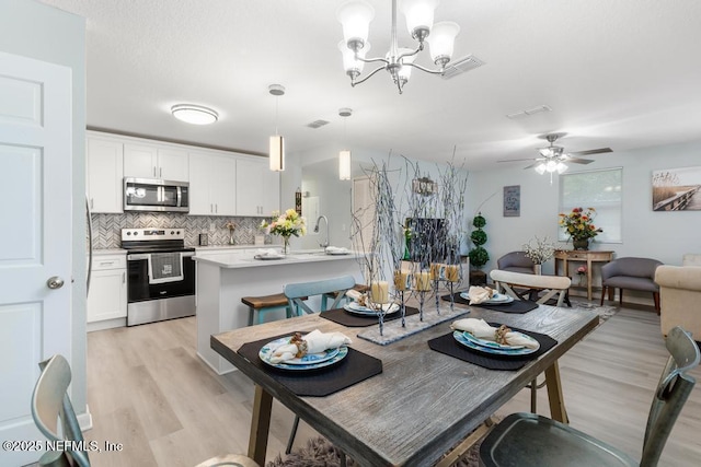 dining space with visible vents, light wood-style flooring, and ceiling fan with notable chandelier