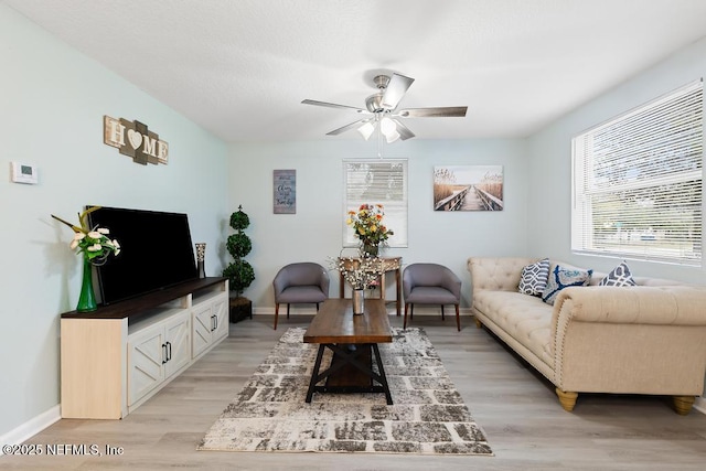 living area with light wood-type flooring, a ceiling fan, and baseboards