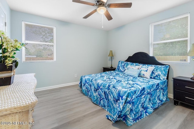 bedroom featuring a ceiling fan, multiple windows, baseboards, and wood finished floors