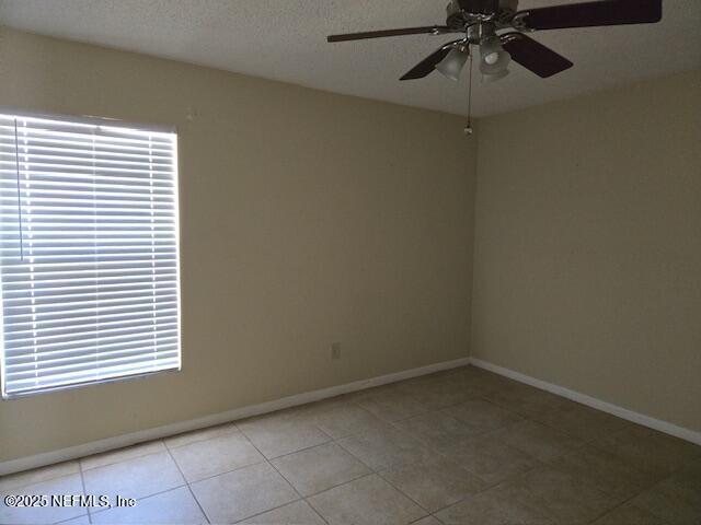 spare room with a textured ceiling, tile patterned flooring, a ceiling fan, and baseboards