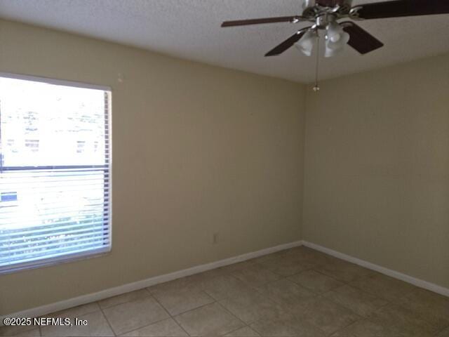 empty room with a textured ceiling, tile patterned floors, a ceiling fan, and baseboards