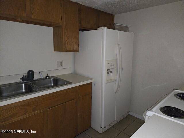 kitchen featuring light tile patterned floors, white appliances, a sink, light countertops, and brown cabinetry