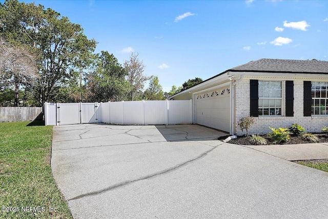 view of side of property featuring brick siding, fence, concrete driveway, a lawn, and a gate