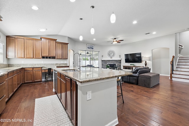 kitchen featuring dark wood finished floors, ceiling fan, light stone counters, a fireplace, and a sink