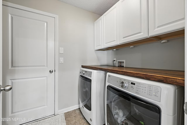 clothes washing area featuring a textured ceiling, independent washer and dryer, cabinet space, and baseboards