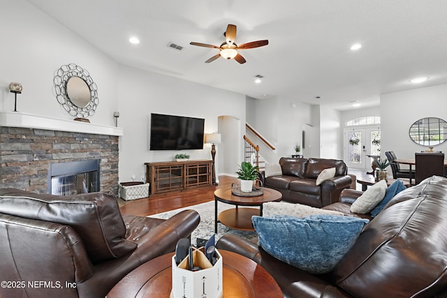 living room with visible vents, ceiling fan, wood finished floors, stairs, and a stone fireplace