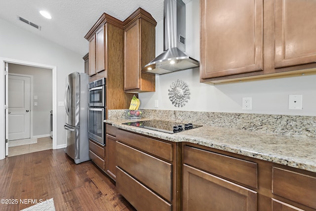 kitchen featuring lofted ceiling, stainless steel appliances, dark wood-style flooring, visible vents, and wall chimney range hood