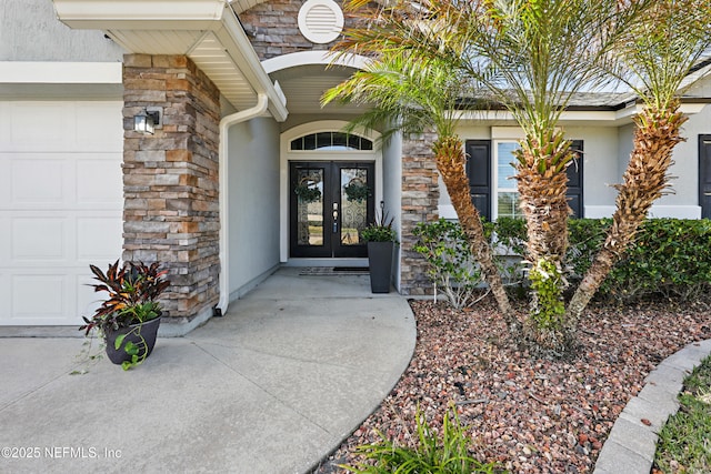 property entrance with an attached garage, stone siding, stucco siding, and french doors